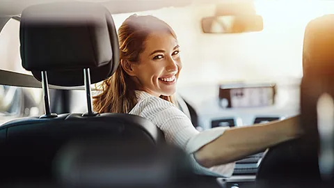 Ehrenamtliche Fahrerin sitzt am Lenkrad im Auto und lächelt mit einem Schulterblick zur Rückbank