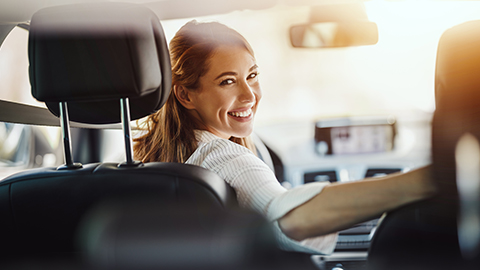 Ehrenamtliche Fahrerin sitzt am Lenkrad im Auto und lächelt mit einem Schulterblick zur Rückbank