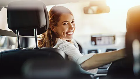 Ehrenamtliche Fahrerin sitzt am Lenkrad im Auto und lächelt mit einem Schulterblick zur Rückbank