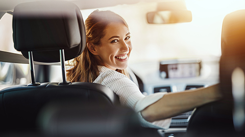 Ehrenamtliche Fahrerin sitzt am Lenkrad im Auto und lächelt mit einem Schulterblick zur Rückbank